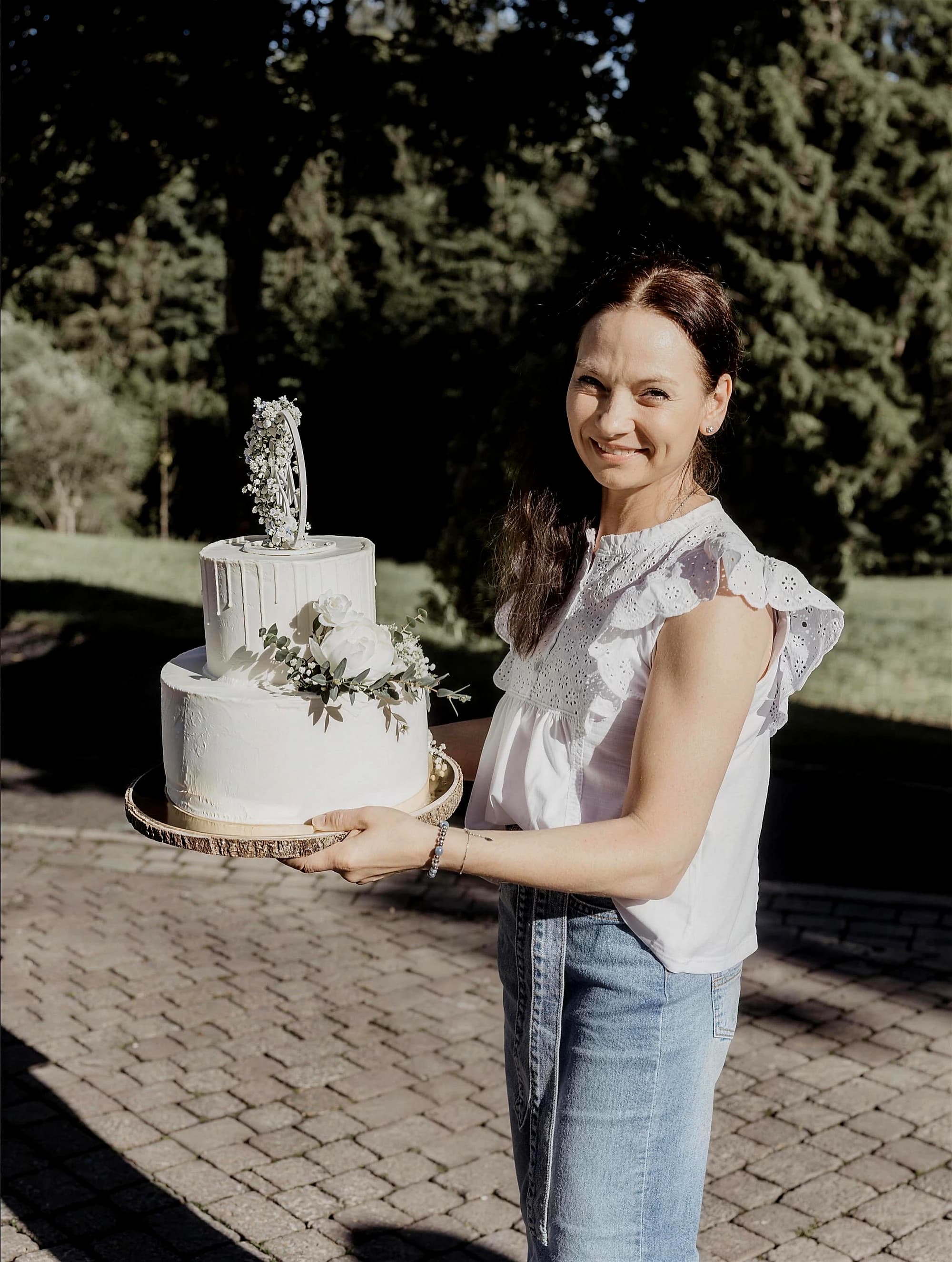 Silvia trägt eine weiße Hochzeitstorte über die Wiese zur Trauung im Freien
