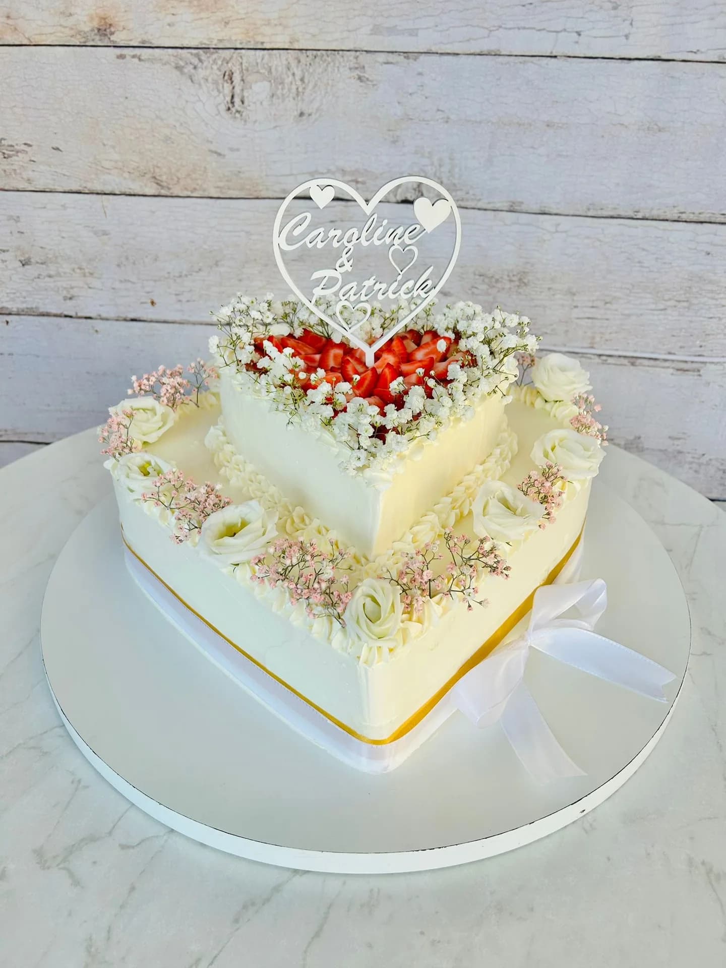 Zweistöckige herzförmige Hochzeitstorte mit Erdbeeren, Schleierkraut und weißen Rosen