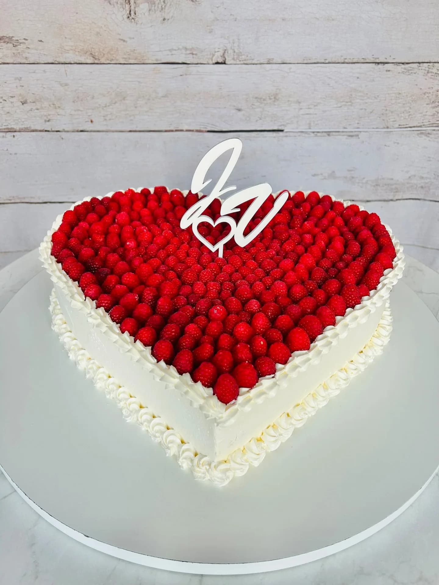 Herzförmige Hochzeitstorte mit frischen Himbeeren und weißem Monogramm-Topper